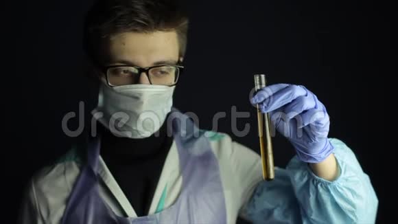 一位戴着一次性口罩戴眼镜的年轻白种人医生看着一个有溶液的灯泡深色背景视频的预览图