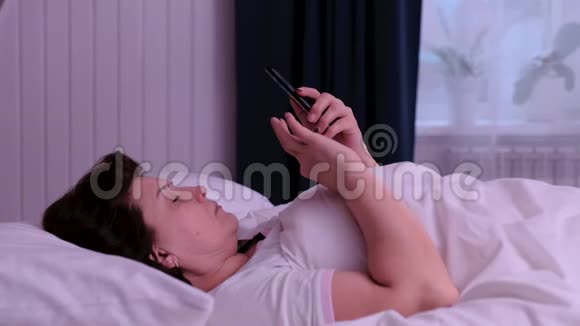 早上躺在床上使用智能手机的成年女性视频的预览图