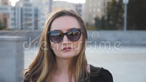 年轻女商人戴太阳镜的肖像背景是城市风景有魅力的商业女性看着摄像机视频的预览图
