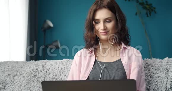 坐在沙发上戴着耳机和笔记本电脑的漂亮女士视频的预览图