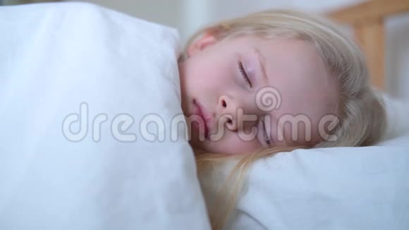 睡着的金发小女孩一大早就躺在大床上铺着白色床上用品孩子们做梦童年平静视频的预览图