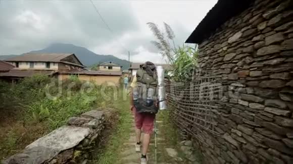 高加索游客徒步旅行者带着背包徒步穿越尼泊尔尼泊尔村后方视野视频的预览图