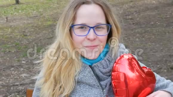 一位金发碧眼戴着眼镜坐在春天公园里微笑的年轻美女的肖像视频的预览图