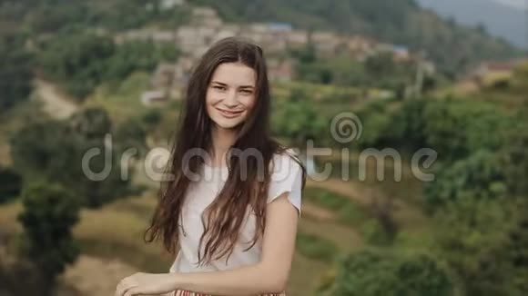 尼泊尔一个年轻的苗条的白种人女孩长着棕色的长发在山顶上对着镜头微笑视频的预览图