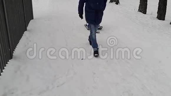 父亲穿着深蓝色的外套拉着小男孩在雪地拖拉机雪橇上的道路上覆盖着雪前景视频的预览图