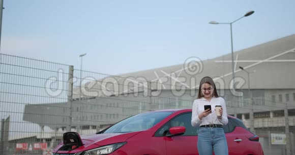 女孩使用智能手机和等待电源连接到电动汽车上充电电池生态视频的预览图