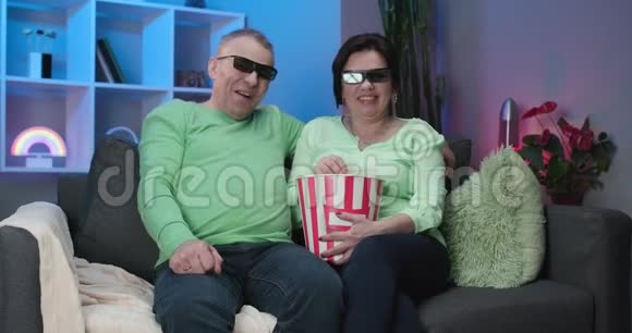 年长的男人和女人一起看电视坐在沙发上看一部迷人的3D眼镜电影高级视频的预览图