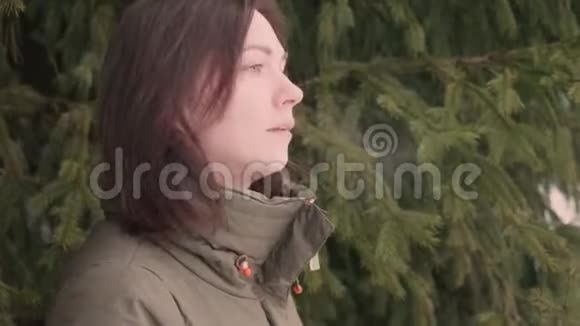 背景为绿色毛皮树的深色头发悲伤而体贴的女人可见气息视频的预览图