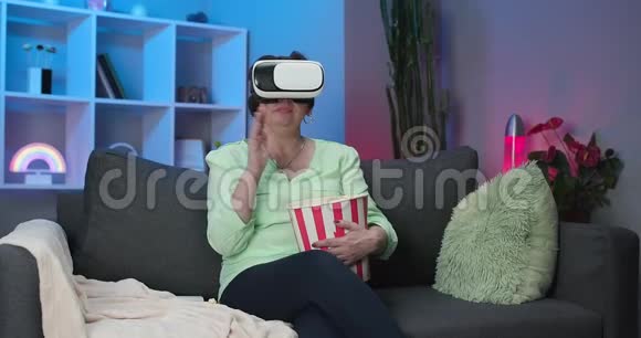 老年女性晚上佩戴VR耳机触摸虚拟屏幕女人坐在沙发上戴着虚拟现实耳机视频的预览图