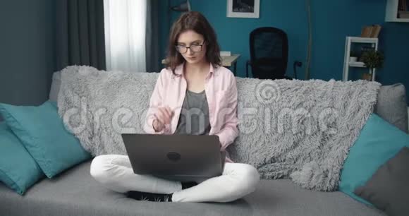戴眼镜的漂亮女孩坐在沙发上用电脑视频的预览图
