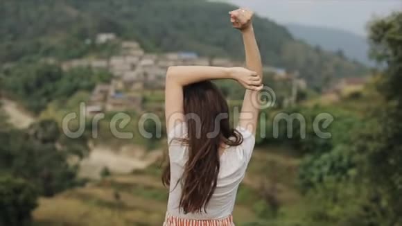一个年轻苗条的白种人女孩长着棕色的长发伸展在尼泊尔的一座山顶上后视景视频的预览图