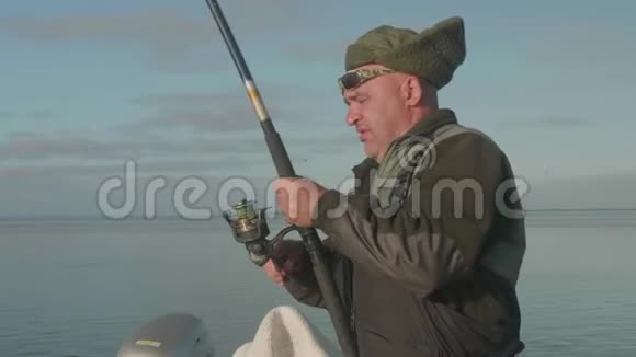 白白种人的渔夫穿着暖和的衣服头上戴着帽子费力地拔出他的鱼竿钓上一条大鱼视频的预览图