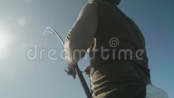 白白种人的渔夫穿着暖和的衣服头上戴着帽子费力地拔出他的鱼竿钓上一条大鱼视频的预览图
