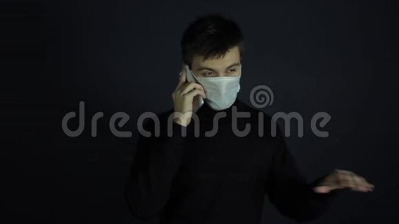 一个年轻的白种人戴着一个防护卫生的医疗面罩在电话里说话冠状病毒保护室内视频的预览图