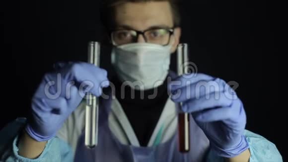一位戴着一次性口罩戴眼镜的年轻白种人医生将两个灯泡与溶液混合深色背景视频的预览图