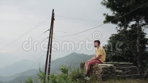 一个年轻的白种人坐在山顶上欣赏尼泊尔美丽的风景视频的预览图