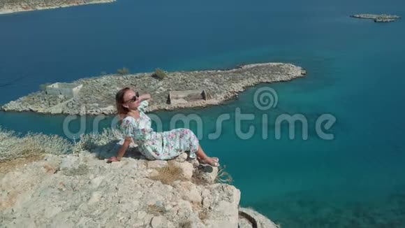 穿裙子的女人坐在海边的悬崖边上视频的预览图