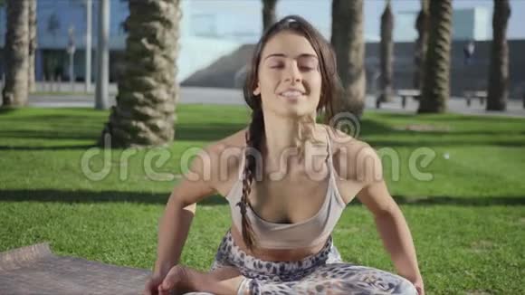 女人在公园里冥想女士坐在户外瑜伽垫上的莲花姿势视频的预览图