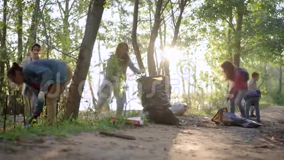 成年妇女在夏天打扫农村森林的土地把废物放进大黑袋里视频的预览图