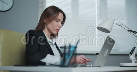 女人坐在办公桌前用笔记本电脑年轻的女商人正坐在办公室里写笔记本视频的预览图