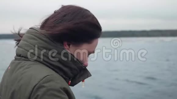站在河背景上的浅黑肤色的妇女的侧景女人不想在大衣领子里藏着冷脸视频的预览图