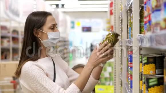 带着带口罩的女孩子的年轻女子在超市买罐头食品视频的预览图
