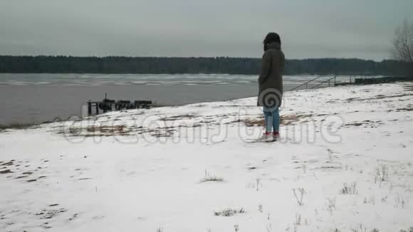 穿着深绿色外套和粉红色运动鞋的布鲁内特站在冰冻的雪岸上视频的预览图
