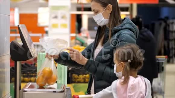 带着女儿戴着医用口罩的女人超市里的秤上有一个称重的橘子视频的预览图