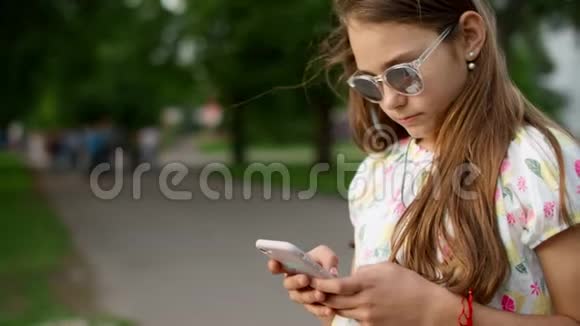 快乐的女孩在公园里打电话玩游戏玩的女孩用智能手机视频的预览图