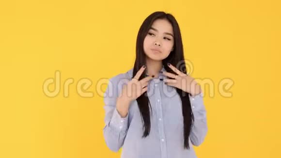 黄色背景的年轻亚洲女孩微笑着看着相机蓝色衬衫视频的预览图