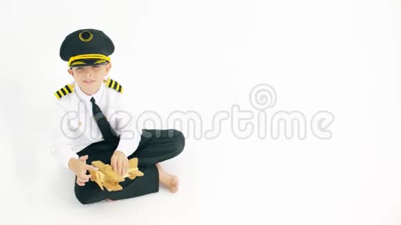 穿着飞行员制服男孩在白色背景上玩普通木制玩具飞机视频的预览图