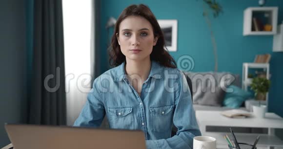 带着笔记本电脑坐在桌子旁的微笑女孩的肖像视频的预览图