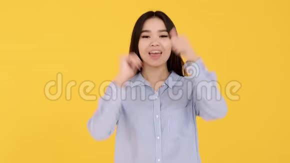 开朗的亚洲女孩穿着蓝色衬衫显示班级两只手在黄色背景上视频的预览图