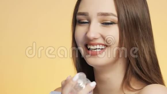 在彩色画室背景下美丽的女孩喜欢瓶子里的香水味一个年轻的女人嗅着笑着视频的预览图