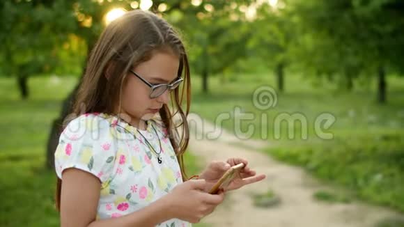 严肃的女孩在电话里玩游戏集中精力的女孩站在夏季公园视频的预览图