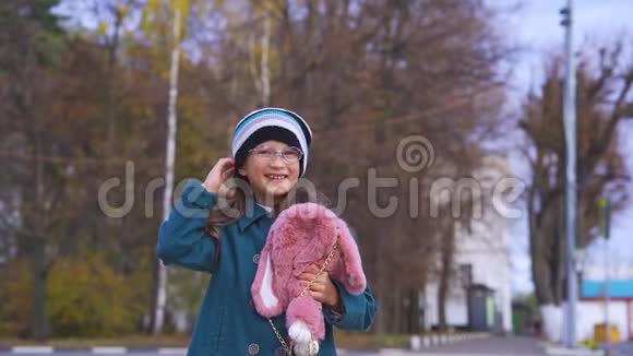 一个带着眼镜穿着一件深绿色外套戴着针织帽子带着背包的粉红色袋子的笑少女的肖像视频的预览图