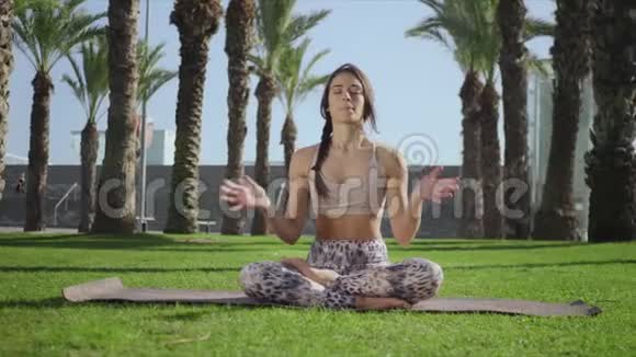 漂亮的女人坐在草地上的莲花姿势在公园练习瑜伽的教练视频的预览图