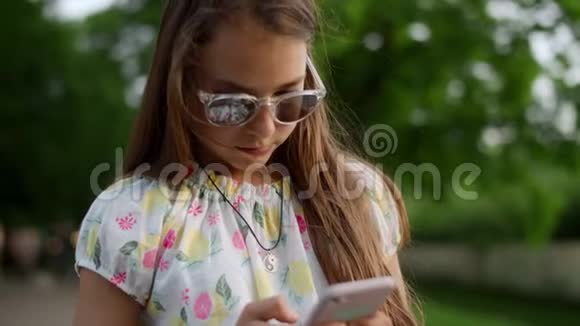 在电话里玩游戏的严肃女孩夏天公园有电话的女孩视频的预览图