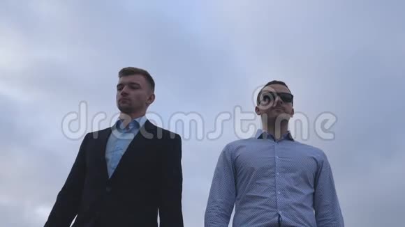 两个年轻的商人在城市里散步背景是蓝天英俊的同事一起上下班视频的预览图