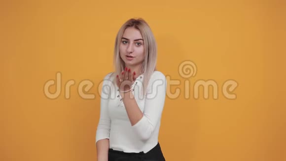 穿着白色t恤的漂亮年轻女子把空气吻隔在橙色的墙上视频的预览图