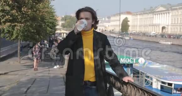 帅哥在等人喝咖啡他穿着黄色的毛衣和黑色的雨衣河堤视频的预览图