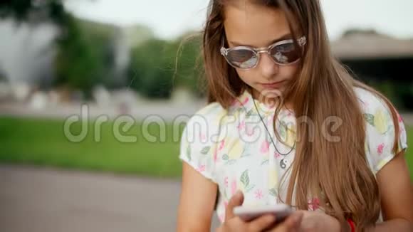 在夏季公园微笑的少女在手机上上网视频的预览图