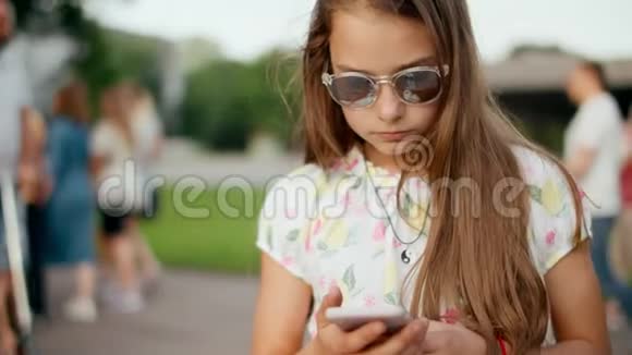 在夏季公园里关闭认真的少女浏览智能手机视频的预览图