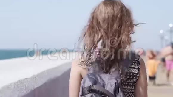 一个女孩带着背包和无线耳机沿着海滨散步视频的预览图