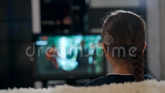 一个年轻女孩坐在沙发上看电视上的电影视频的预览图