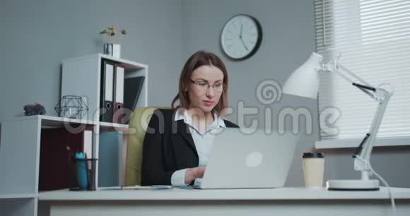 年轻美丽的布鲁内特工作在笔记本电脑在酷创意机构在一个阁楼办公室她有一杯外卖咖啡视频的预览图