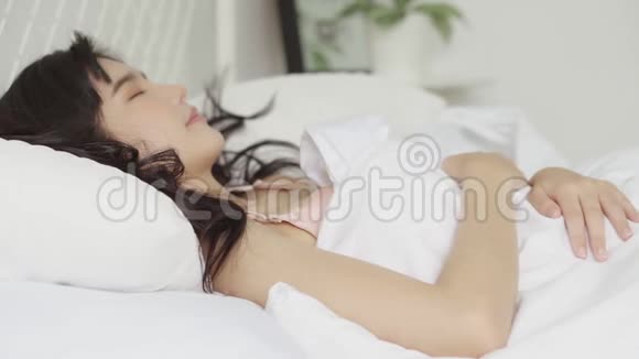 美丽的亚洲年轻女子躺在床上头靠在枕头上舒适而快乐地躺在卧室里视频的预览图
