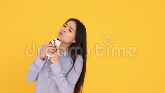 戴着黄色背景耳机的亚洲女孩在电话里唱卡拉OK跳舞视频的预览图