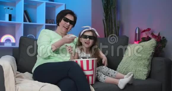 一个带着一个小女孩的老年妇女戴着3D眼镜看电视和吃爆米花老前辈老奶奶视频的预览图