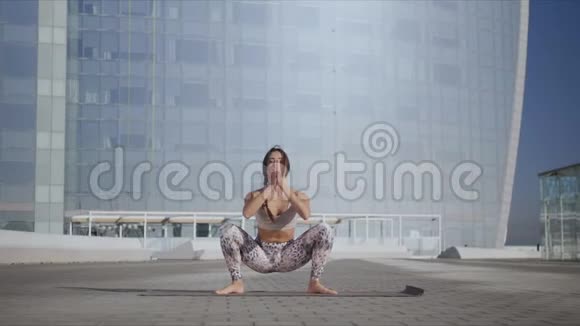 在街上的瑜伽垫上做花环姿势的女人瑜伽教练在户外锻炼视频的预览图